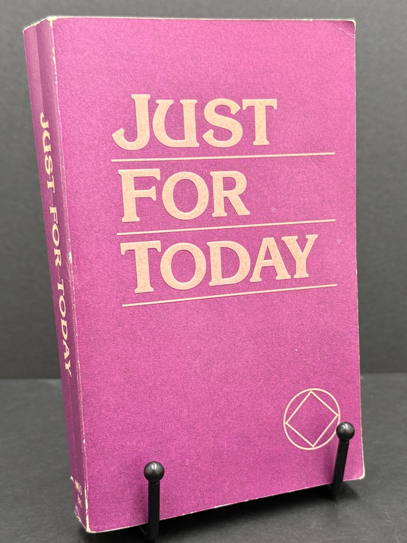 A vintage book titled 'Just For Today' with a textured magenta-purple cover and cream-colored lettering, displayed on a small black stand against a dark gray background.